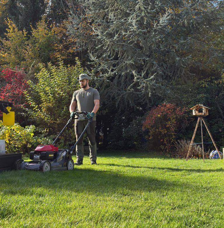 Gartenpfleger mäht eine Rasenfläche mit einem Rasenmäher in einem privaten Garten.